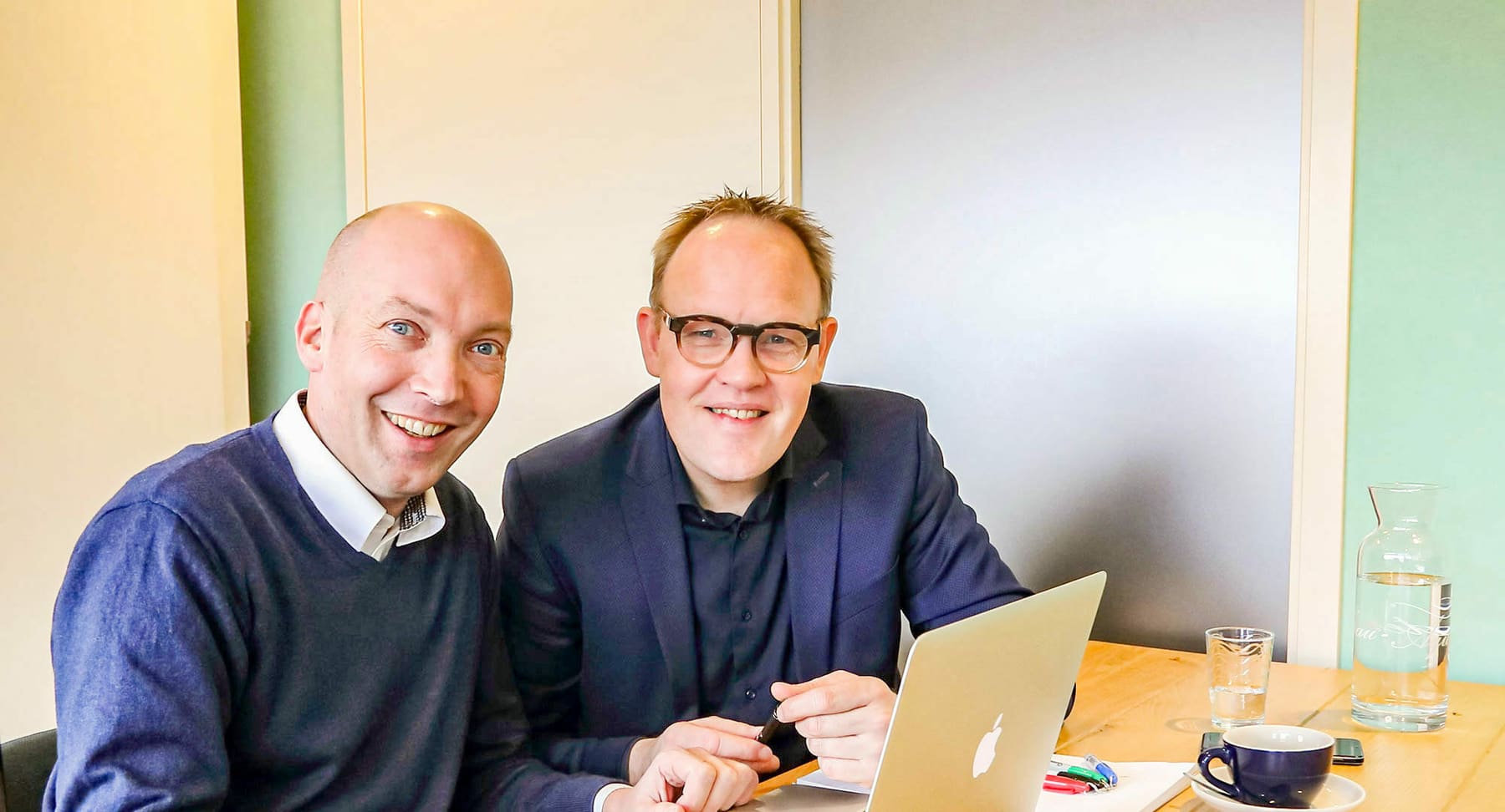 Twee adviseurs van Bloedjes & Eriks lachen samen aan tafel bij een laptop