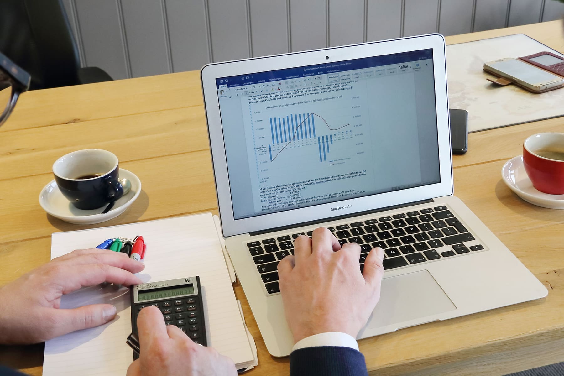 Handen met een rekenmachine naast een laptop met een grafiek