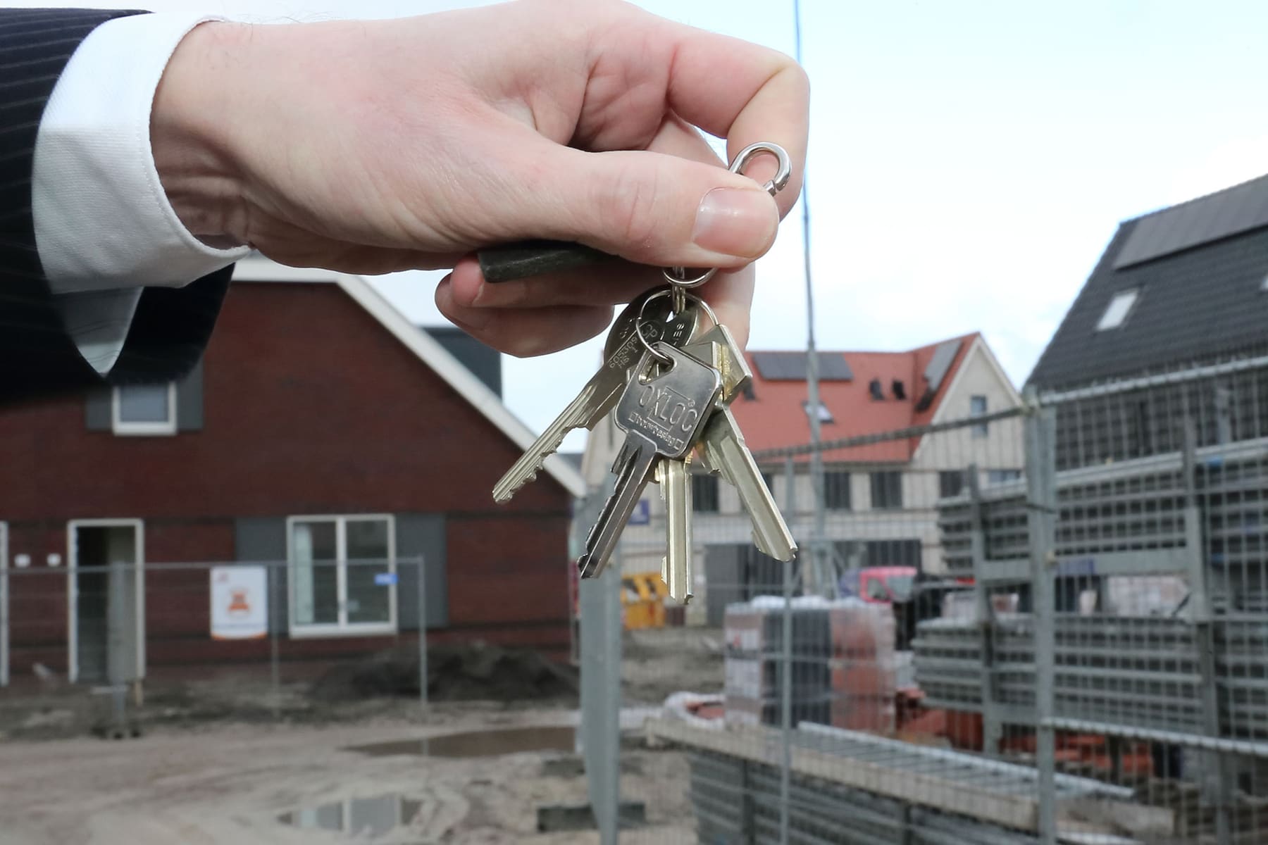 Hand met huissleutels voor een rij nieuwbouwwoningen